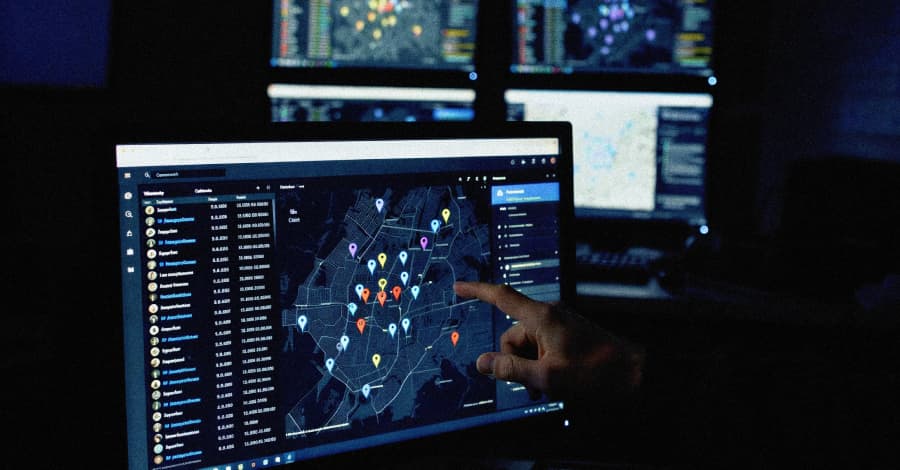 Un operador señala un mapa digital con marcadores de ubicación, simbolizando el rastreo masivo de datos y la vigilancia de dispositivos, en un centro de monitoreo.