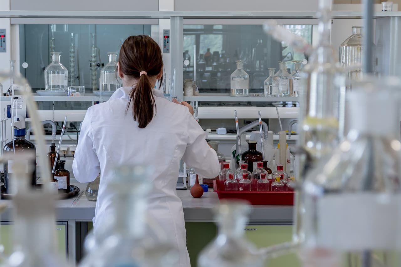 Una científica trabajando de espaldas en un laboratorio químico rodeada de material de vidrio y equipos de investigación.